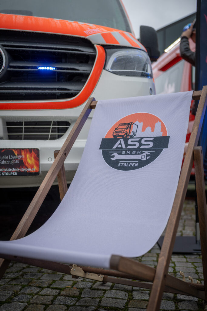 Liegestuhl mit ASS-Logo vor einem orangefarbenen Feuerwehrfahrzeug