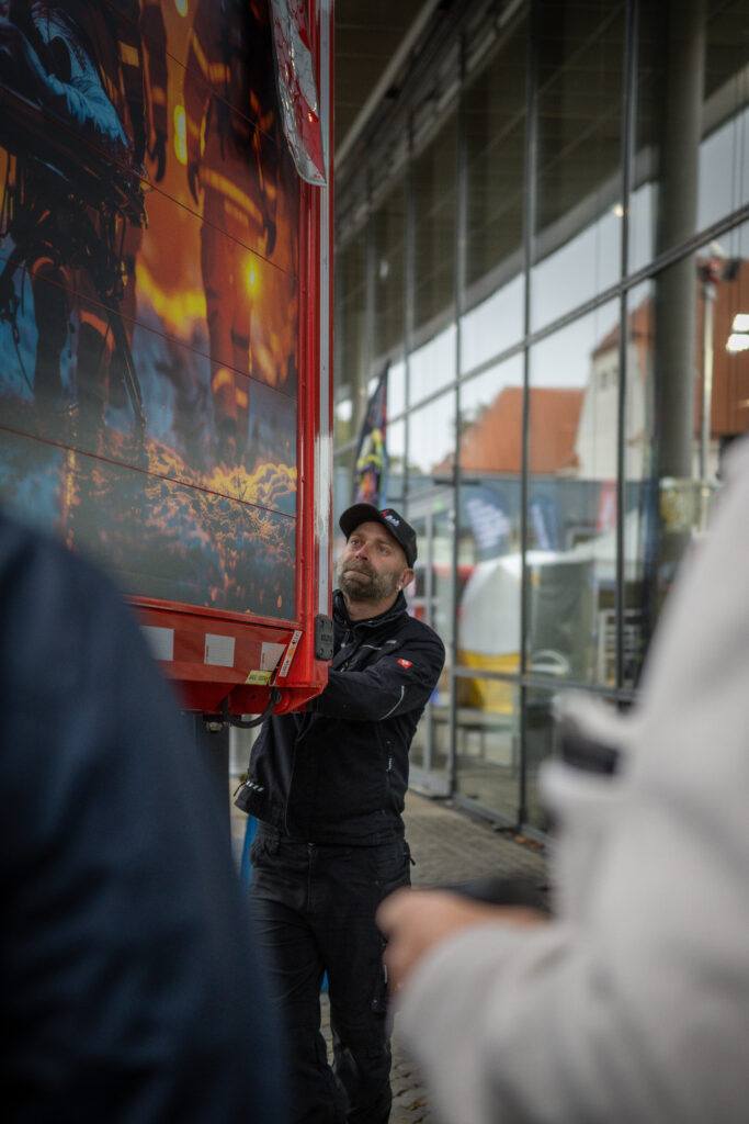 Mitarbeiter öffnet die hochklappbare Seitenwand eines roten Lkw-Aufbaus