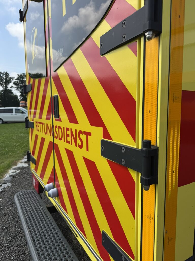 Gelber Rettungswagen mit Warnmarkierung, Notrufnummer 112 und blauem Signalbalken